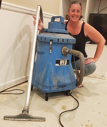 Beth crouching behind a big blue shop vac